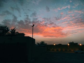 Street by silhouette buildings against sky during sunset