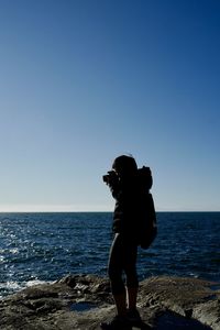 Rear view of woman standing at beach against clear blue sky