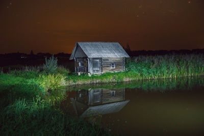 Reflection of plants and house in lake against sky at night