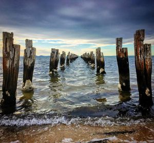 Wooden posts in sea against sky