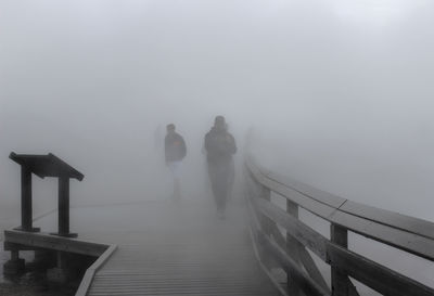 People walking on footbridge in foggy weather