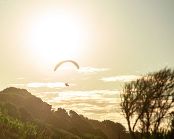 Low angle view of person paragliding against sky at sunset time