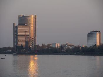 Modern buildings by river against sky in city