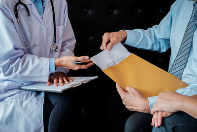 Midsection of doctor discussing with patient while sitting on sofa in hospital