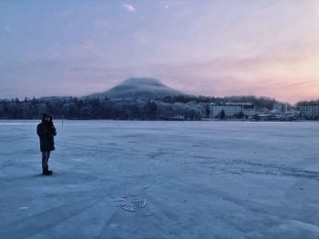 Man standing on frozen lake against sky during winter