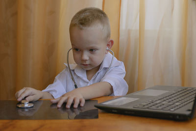 Boy wearing stethoscope while using laptop at table