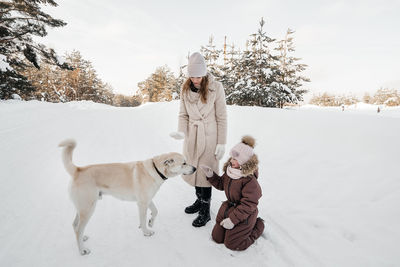 Mother and daughter playing with the dog in the winter forest