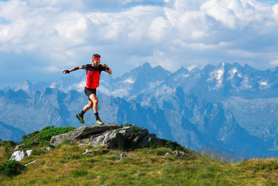 Rear view of man jumping on mountain against sky