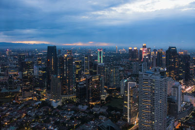 Illuminated buildings in city against cloudy sky