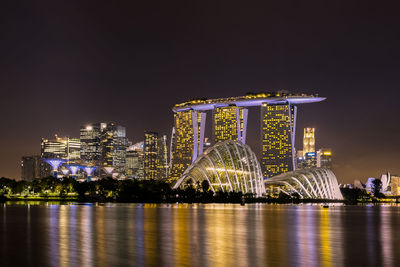 Illuminated city by river against sky at night