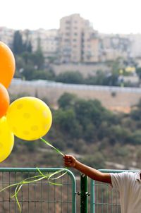 Boy holding balloons against sky in city