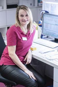 Smiling pharmacist sitting at desk in pharmacy store