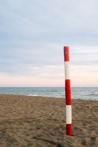 Red and white striped bamboo on shore at beach against sky