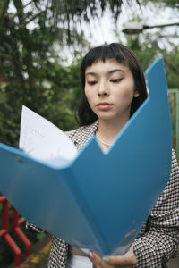 Young woman holding book while standing on paper