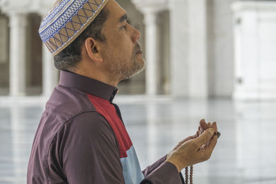 Side view of mature man praying while kneeling at mosque