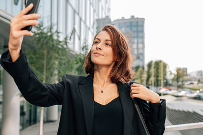 Portrait of young woman standing against buildings in city