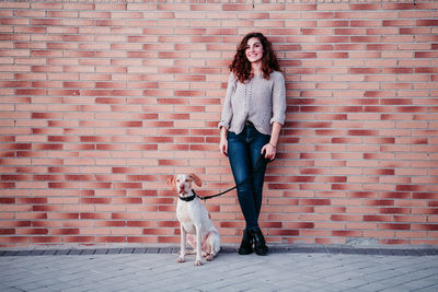 Woman with dog standing against brick wall