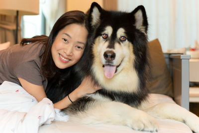 Portrait of smiling woman relaxing with dog on bed at home