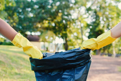 Cropped hands wearing gloves holding garbage bag at park