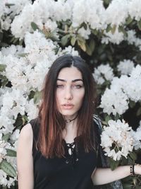 Portrait of young woman standing against flowers