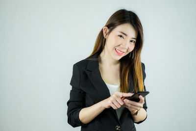 Portrait of smiling young woman using phone against white background