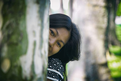 Portrait of woman peeking from behind tree