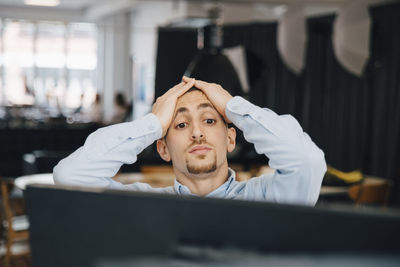 Exhausted computer programmer with head in hands looking at computer while working in office