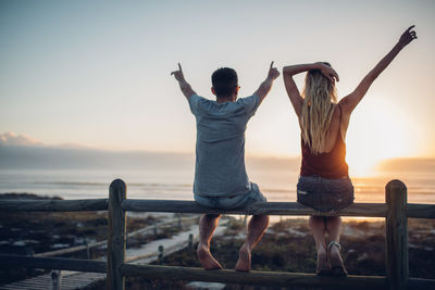 Friends standing by railing against sea during sunset