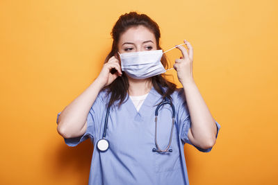 Young woman holding condom while standing against yellow background