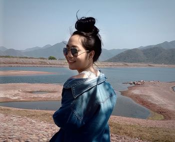 Side view of smiling young woman standing by sea against clear sky