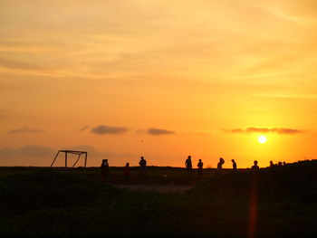 Silhouette people on field against sky during sunset