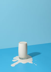 Glass of milk on a blue background in bright light. spilled milk puddle and glass of milk.