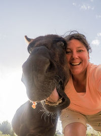 Portrait of smiling young woman with horse against sky