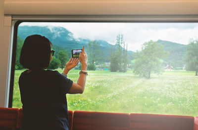 Rear view of woman photographing field from train