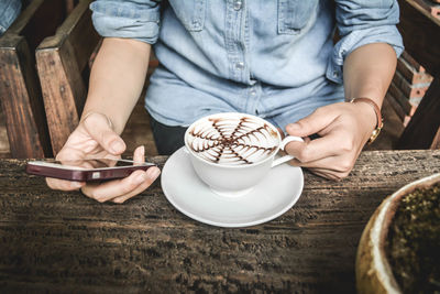 Midsection of person holding hot chocolate and using smartphone