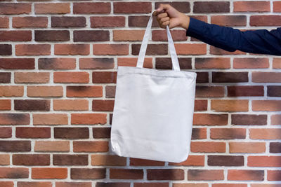 Midsection of person holding umbrella against brick wall