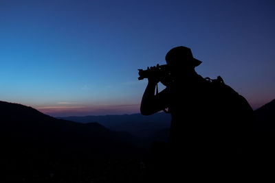 Silhouette man photographing on mountain against sky during sunset