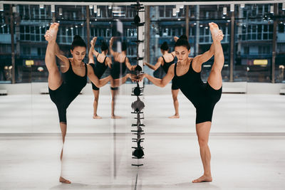 Full length of woman stretching while standing by mirror at gym