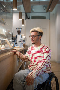 Interested disabled hipster man on wheelchair choosing dessert in cafe looks shop window with cakes