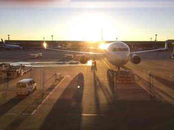 Airplane at airport runway against sky during sunset