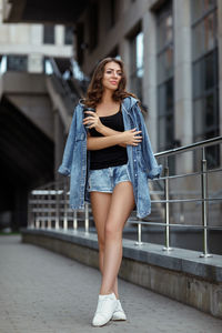 Portrait of young woman standing against building