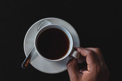 Close-up of hand holding coffee cup against black background