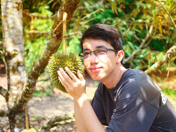 Portrait of young man holding fruit growing on tree