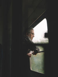 Side view of man looking through window