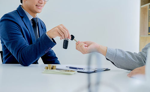Midsection of insurance agent giving keys to client at table in office