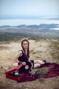 Young woman lies in nature in a black dress next to an old gramophone and listens to music