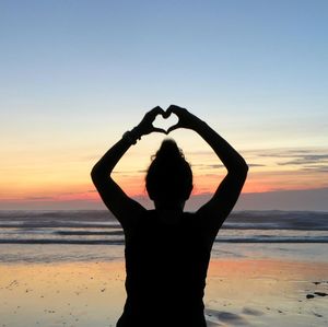 Silhouette woman standing at beach against sky during sunset