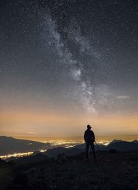 Rear view of silhouette man photographing on mountain against star field at night