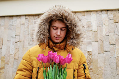 Blond man in a yellow winter jacket with a bouquet of tulips in hands