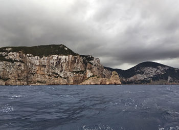 Scenic view of sea by mountain against sky